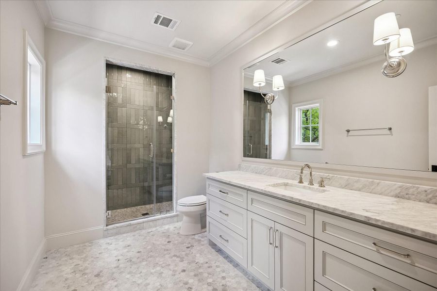 Well-appointed ensuite bath featuring mosaic Carrara tile flooring, marble slab counters, custom cabinetry, and a spacious frameless glass-enclosed shower with gorgeous contrasting tile to the ceiling that adds visual interest. Clean, classic finishes create a bright and functional space.  The window in this bathroom adds wonderful natural light!!!