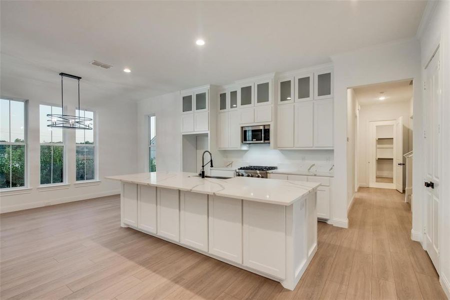 Kitchen featuring recessed lighting, white cabinetry, a center island with sink, decorative light fixtures, and light wood-style floors