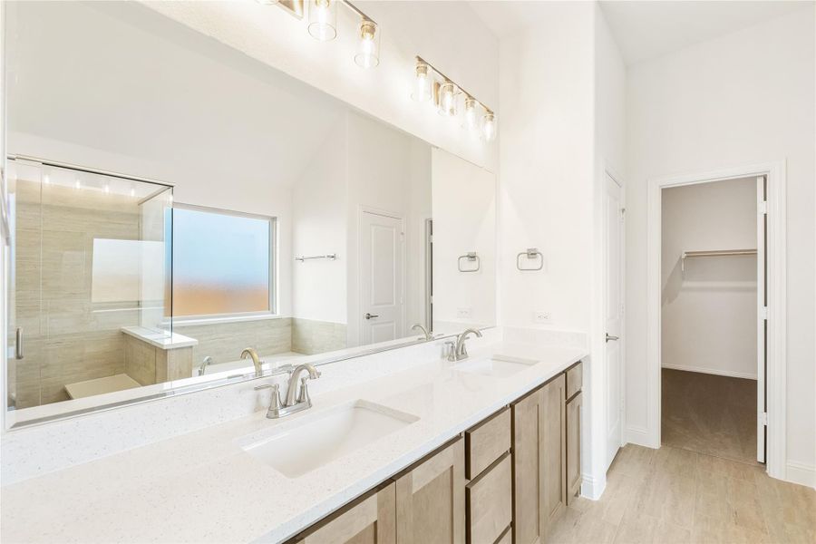 Ensuite bathroom with double sink vanity, large mirror, glass shower, and walk-in closet doorway Ensuite bathroom with double sink vanity, large mirror, glass shower, and walk-in closet doorway