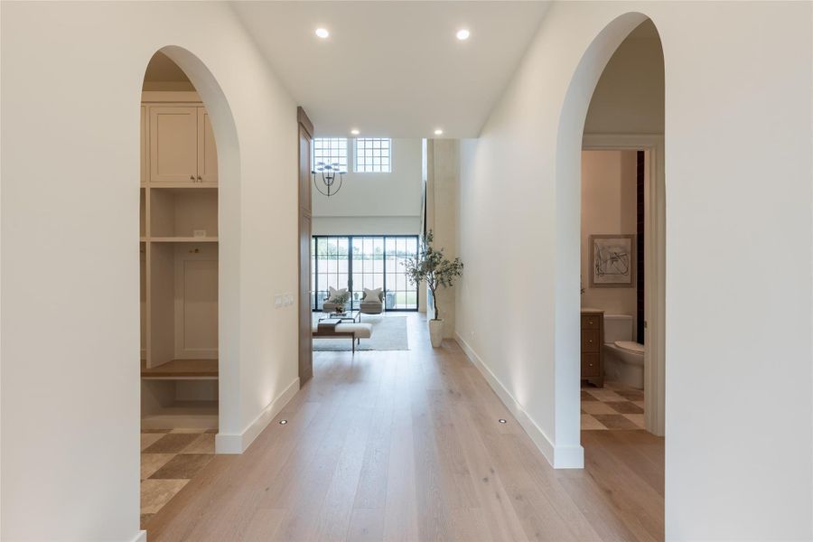 This entry hallway highlights Elevare’s signature use of symmetry and curve, where arched transitions and inset step lights lead the eye to the custom iron front door. European white oak floors ground the space with quiet luxury, while soft uplighting and clean detailing amplify the home’s refined architectural rhythm. This entry hallway highlights Elevare’s signature use of symmetry and curve, where arched transitions and inset step lights lead the eye to the custom iron front door. European white oak floors ground the space with quiet luxury, while soft uplighting and clean detailing amplify the home’s refined architectural rhythm.