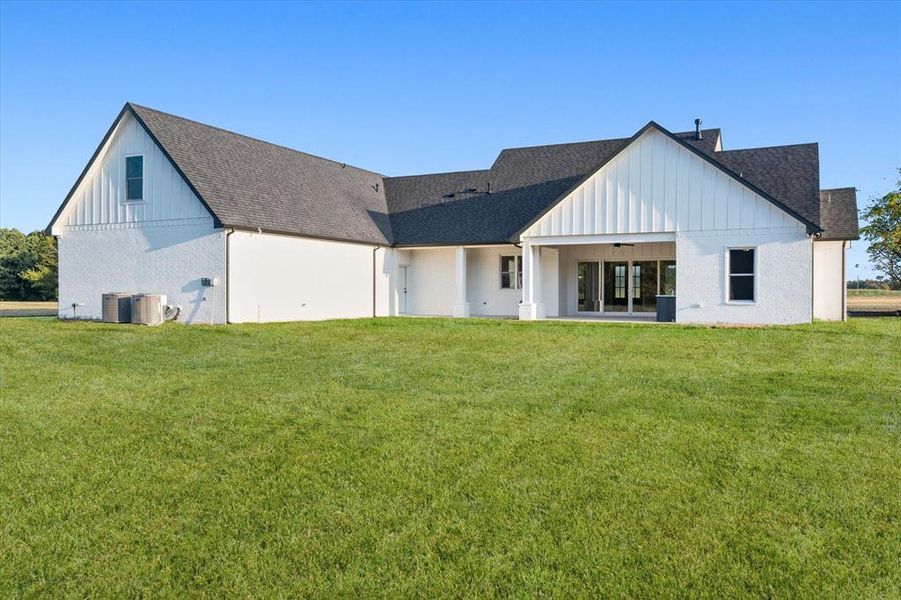 Rear view of house with roof with shingles, a lawn, and board and batten siding Rear view of house with roof with shingles, a lawn, and board and batten siding