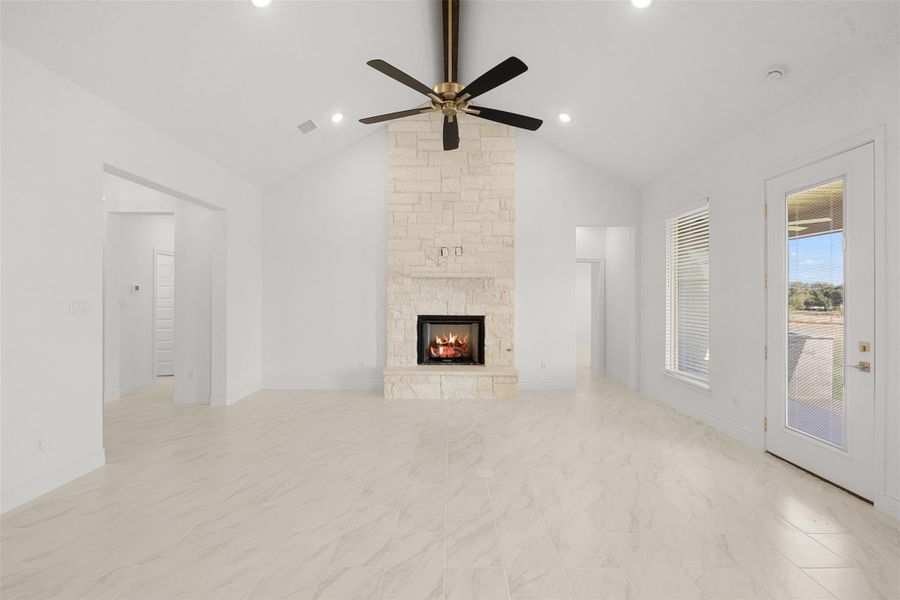 Unfurnished living room featuring ceiling fan and a stone fireplace