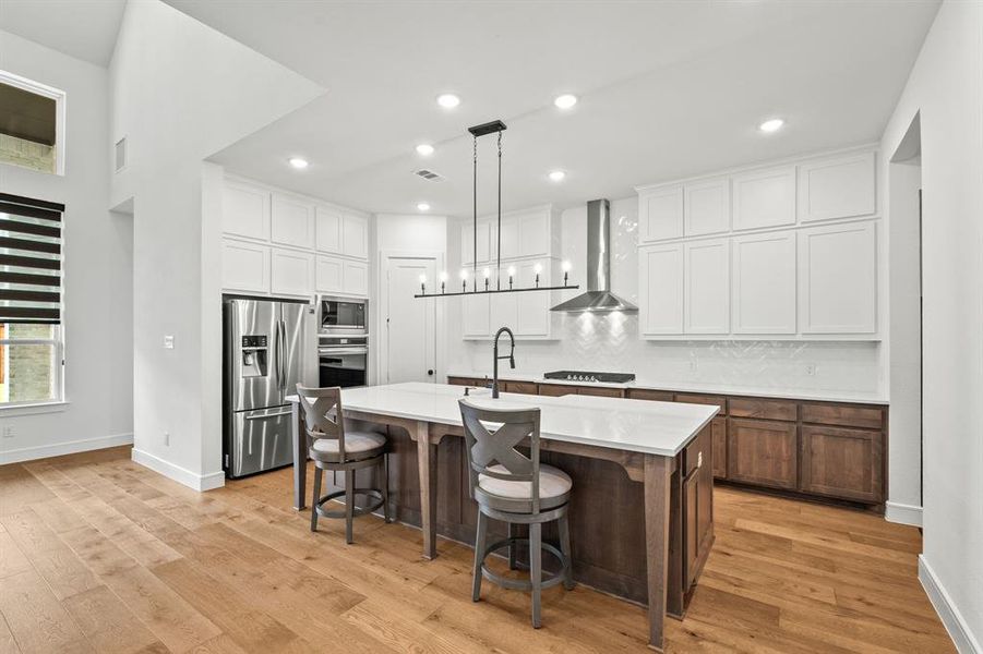 Kitchen with decorative light fixtures, light wood-style flooring, appliances with stainless steel finishes, recessed lighting, and a kitchen bar Kitchen with decorative light fixtures, light wood-style flooring, appliances with stainless steel finishes, recessed lighting, and a kitchen bar