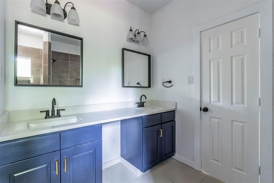 Full bath with double vanity, tile patterned floors, and baseboards Full bath with double vanity, tile patterned floors, and baseboards