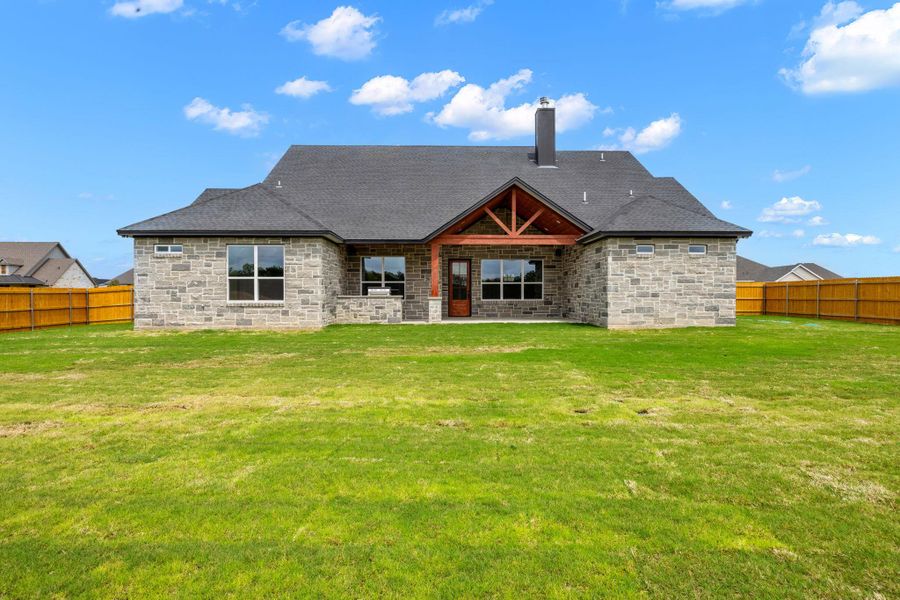 Back of property featuring a fenced backyard, a patio, a chimney, and stone siding
