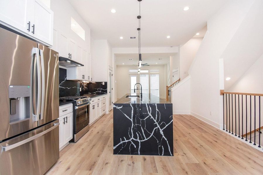 This photo showcases a modern kitchen with sleek stainless steel appliances, white cabinetry, a striking black marble island, and light wood flooring. The open layout is accentuated by high ceilings and ample natural light.