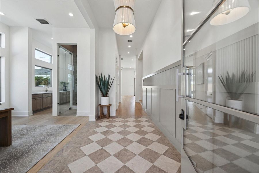 An impressive first impression awaits beyond the stunning front door, where a two-tone checkerboard floor, refined fluted millwork, and a statement chandelier set the tone.