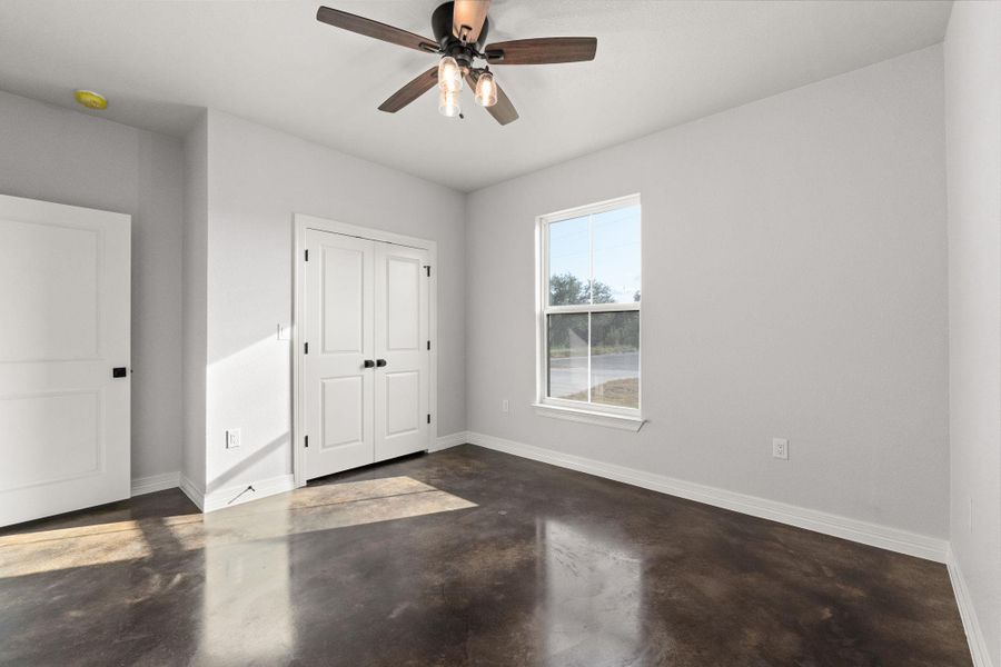 Unfurnished bedroom featuring finished concrete flooring, a ceiling fan, and a closet