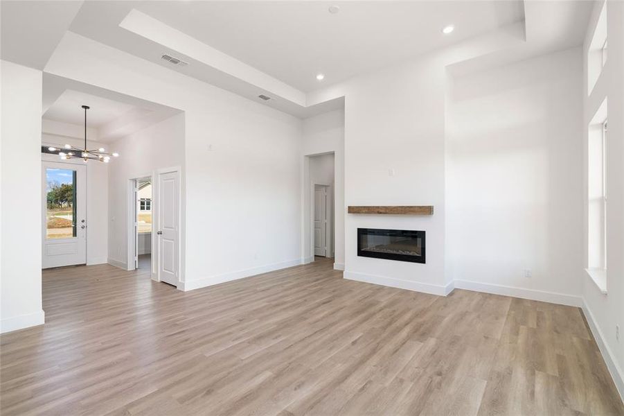 Unfurnished living room with a notable chandelier, light hardwood / wood-style flooring, a high ceiling, and a tray ceiling