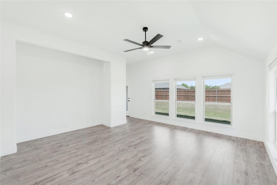 Open living room with vaulted ceiling, ceiling fan, light wood floors, and large windows overlooking backyard Open living room with vaulted ceiling, ceiling fan, light wood floors, and large windows overlooking backyard