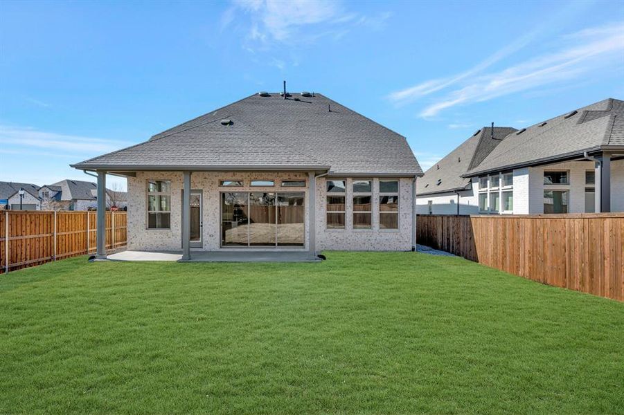 Rear view of house featuring a patio, roof with shingles, brick siding, and a fenced backyard