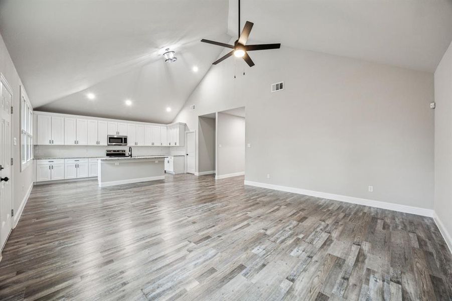 Unfurnished living room featuring high vaulted ceiling, light wood finished floors, and ceiling fan