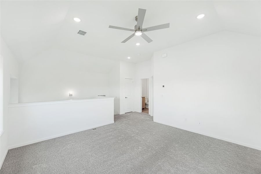Empty bedroom with gray carpet, vaulted ceiling, ceiling fan, and doorway to ensuite bathroom
