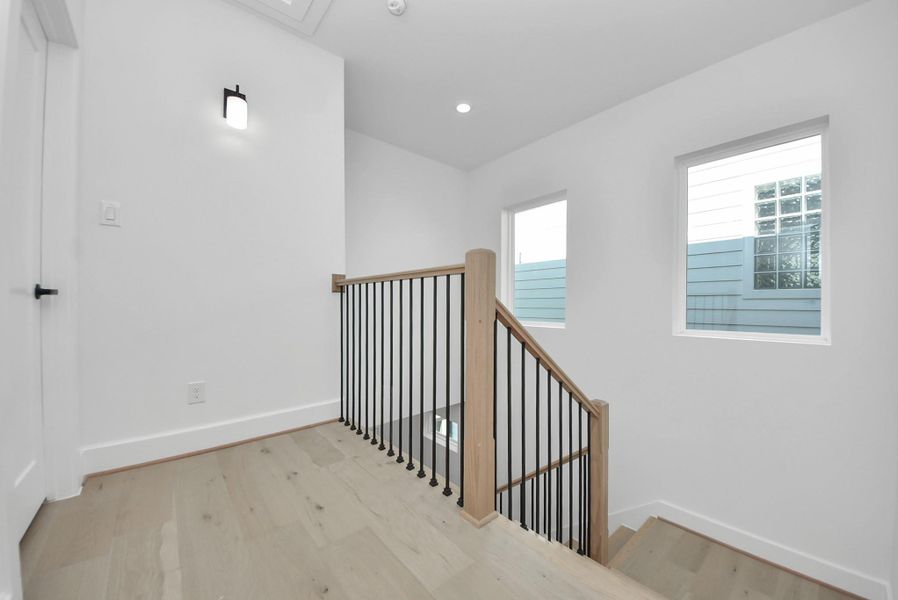 This bright, modern stairway landing features light wood flooring and a sleek black metal railing. Two large windows flood the space with natural light, creating an open and inviting atmosphere. This bright, modern stairway landing features light wood flooring and a sleek black metal railing. Two large windows flood the space with natural light, creating an open and inviting atmosphere.