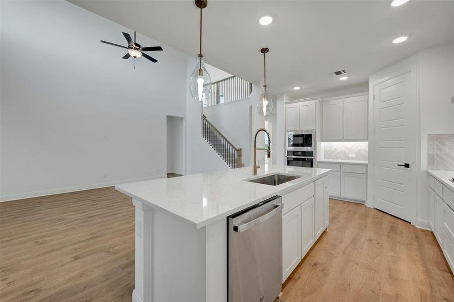 Kitchen with stainless steel appliances, white cabinets, light wood-style flooring, an island with sink, and light stone counters