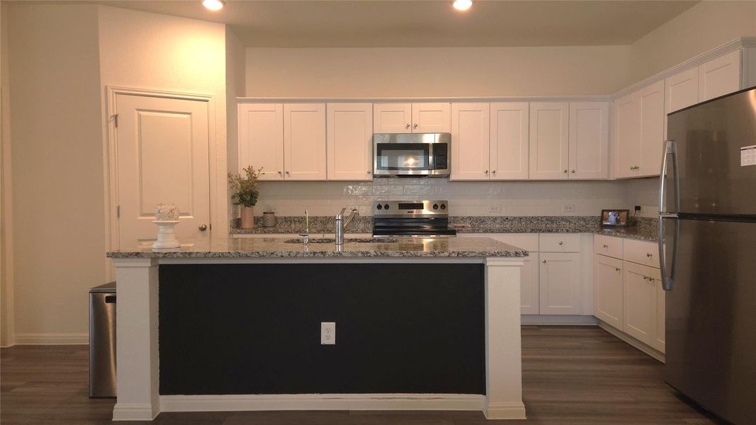 Contemporary kitchen featuring white cabinetry, a dark accent island, stainless steel appliances, speckled countertops, and wood-finish flooring