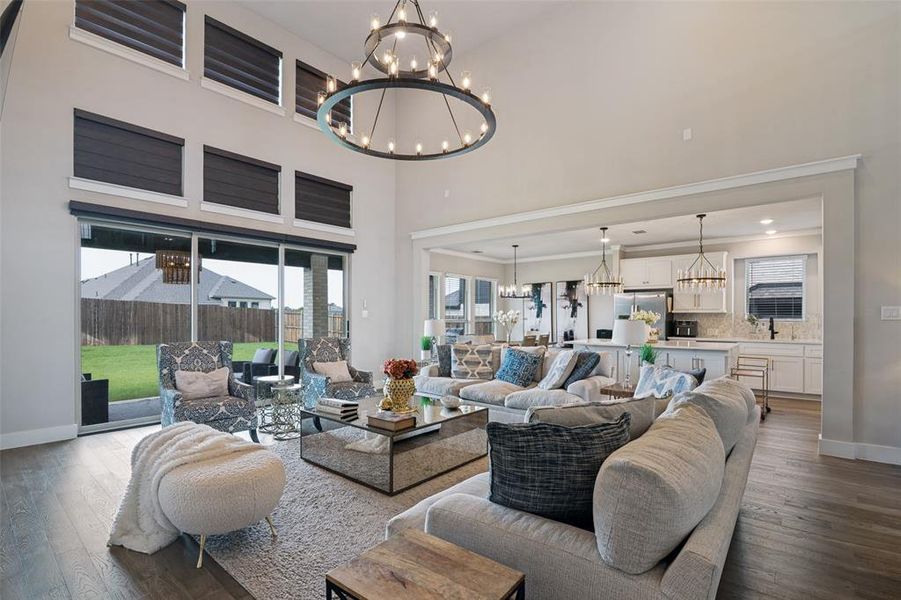 Spacious living area featuring a vaulted ceiling, wood-finish flooring, a large circular chandelier, and expansive sliding glass doors opening to the backyard