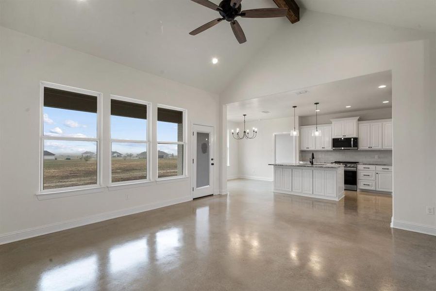 Unfurnished living room featuring high vaulted ceiling, beam ceiling, sink, and ceiling fan with notable chandelier