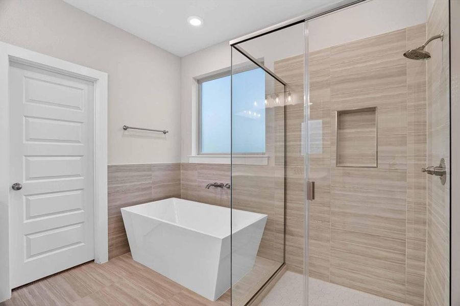 Modern bathroom featuring a frameless glass shower enclosure, a freestanding soaking tub, large format tile flooring, and a tiled shower surround with a recessed niche