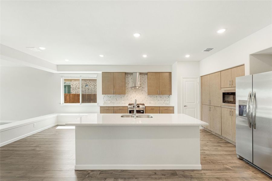 Open kitchen with large white island, light wood cabinets, stainless steel appliances, and wood-look floors