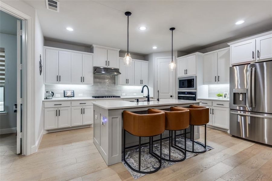 Kitchen with stainless steel appliances, a kitchen breakfast bar, an island with sink, and light wood-style floors