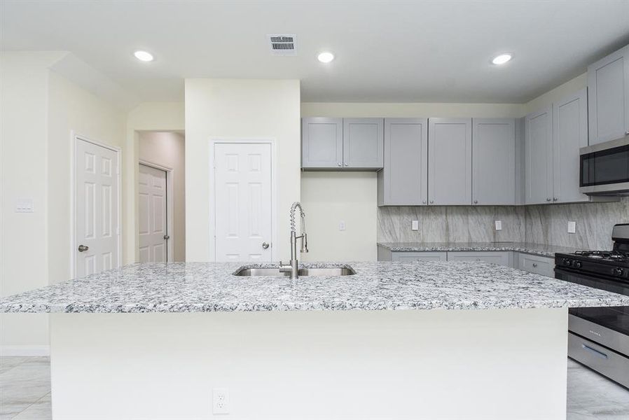 Modern kitchen interior with light gray cabinets, granite countertops, stainless steel appliances, and neutral wall colors.