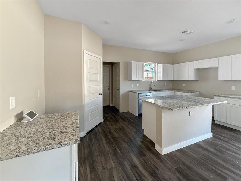 Kitchen with light stone counters, dark wood-style floors, a kitchen island, and white cabinetry