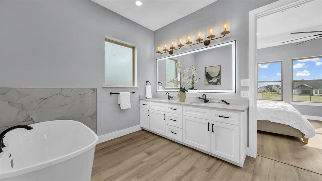 Full bathroom with double vanity, a soaking tub, light wood finished floors, ensuite bathroom, and a ceiling fan