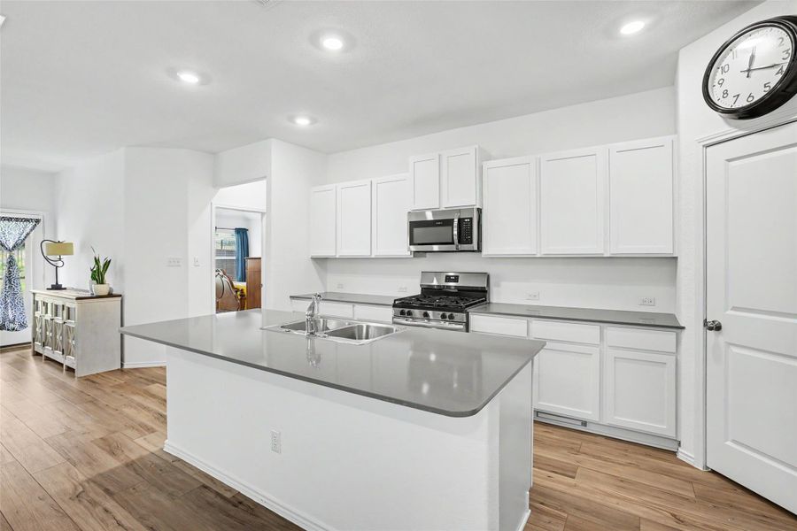 Modern kitchen featuring an island with an undermount double basin sink, white cabinetry, stainless steel appliances, and wood-finish flooring