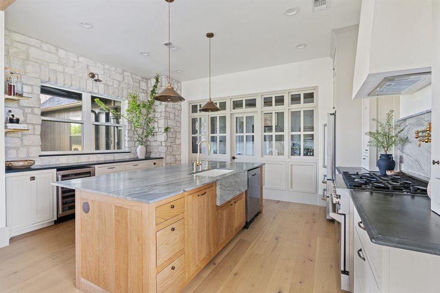 Kitchen featuring custom range hood, light hardwood / wood-style floors, beverage cooler, a kitchen island with sink, and sink