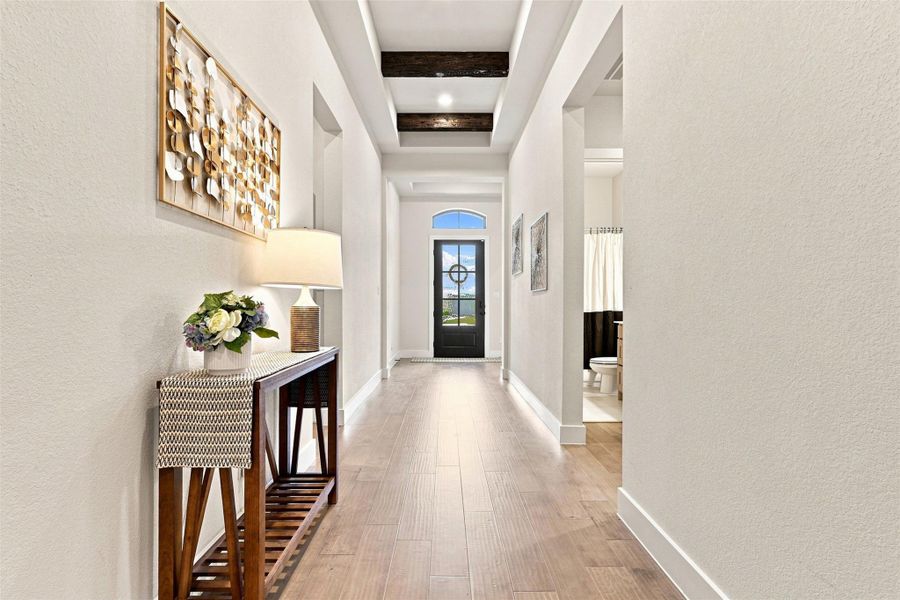 A graceful entry hall welcomes guests with light faux-wood tile floor and distinctive exposed beam accents.