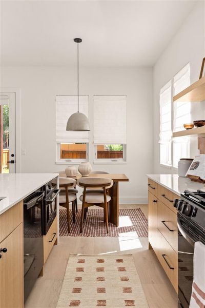 Kitchen with black appliances, decorative light fixtures, light stone countertops, light wood-style floors, and modern cabinets