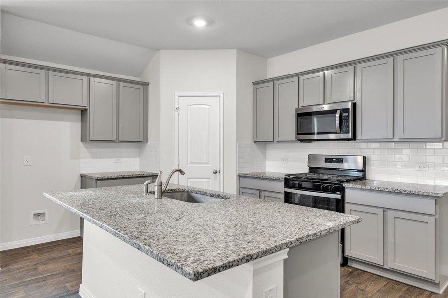 The kitchen features a center island with a sink, grey cabinetry, granite countertops, and a subway tile backsplash