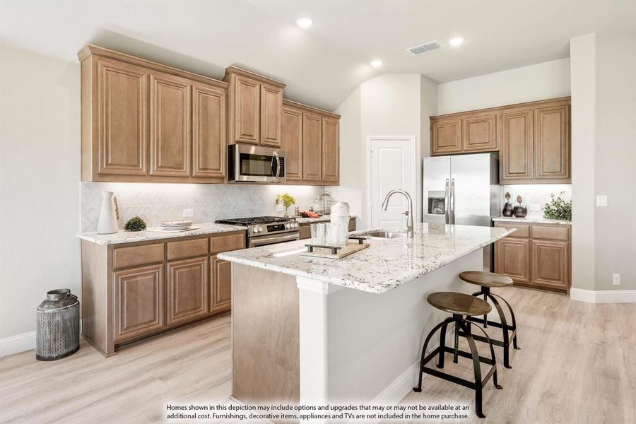 Kitchen with brown wood cabinets, granite island with sink, stainless steel appliances, and light hardwood floors
