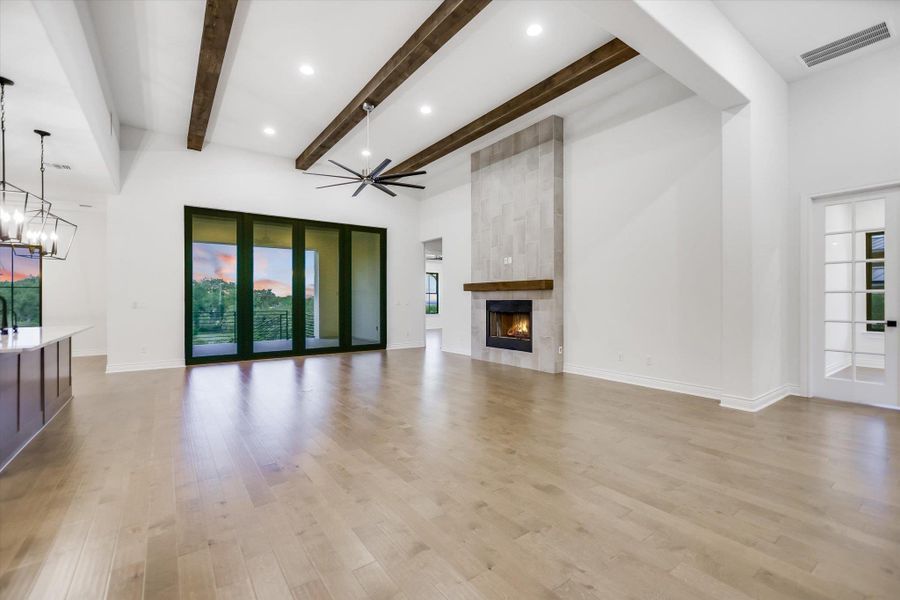 Living room featuring a tile fireplace, a chandelier, beamed ceiling, light wood-style floors, and a towering ceiling