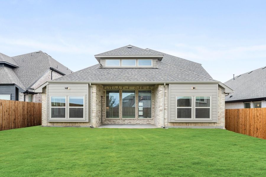 Rear exterior of single-story brick home with hip roof, covered patio, large windows, and fenced backyard lawn Rear exterior of single-story brick home with hip roof, covered patio, large windows, and fenced backyard lawn