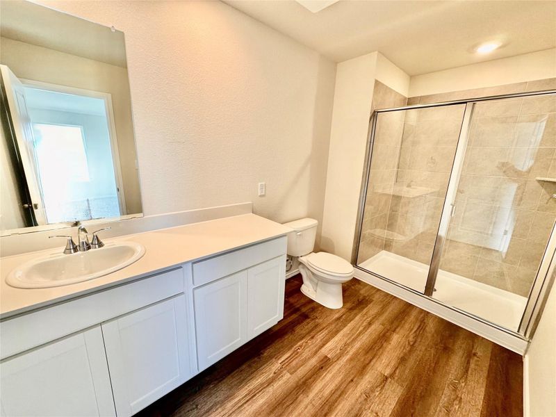 Bathroom with vanity, a shower stall, dark wood-style floors, and a textured wall Bathroom with vanity, a shower stall, dark wood-style floors, and a textured wall