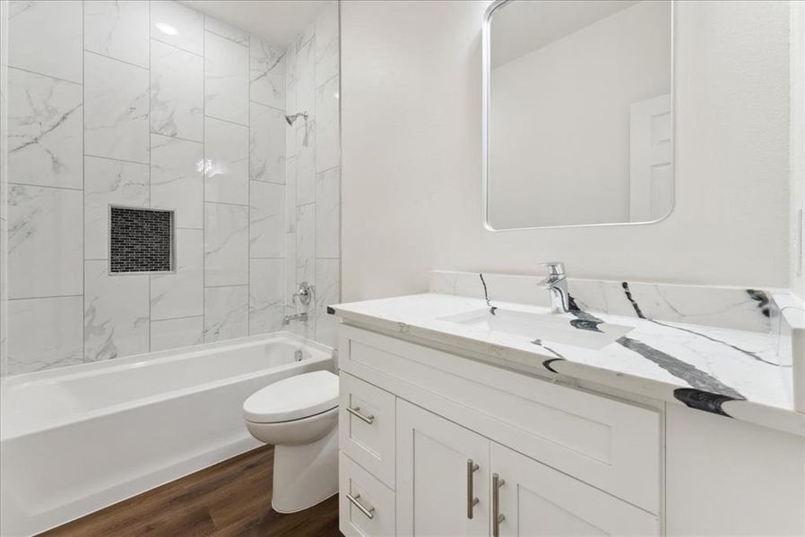 Full bathroom featuring toilet, vanity,wood style vinyl floors, and tiled shower / bath combo