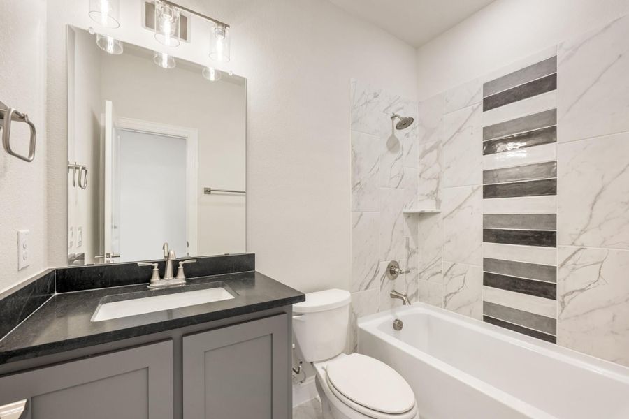 Bathroom with gray vanity, dark countertop, and tub-shower combo with marble-look tile and gray accent strips Bathroom with gray vanity, dark countertop, and tub-shower combo with marble-look tile and gray accent strips