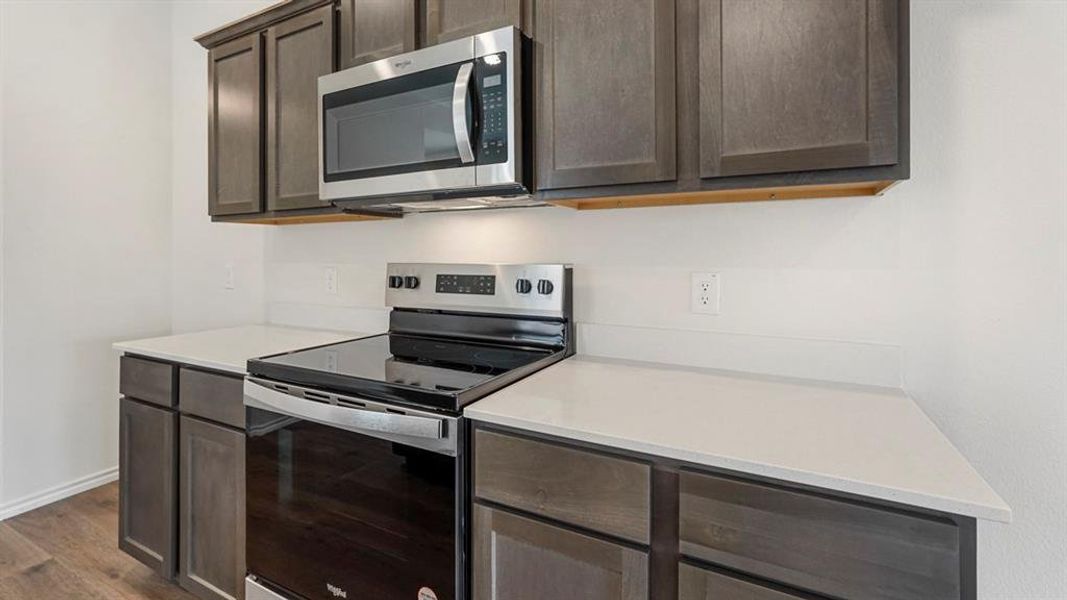Kitchen featuring a stainless steel electric range, a stainless steel over-the-range microwave, dark wood-finish cabinetry, and light-toned countertops
