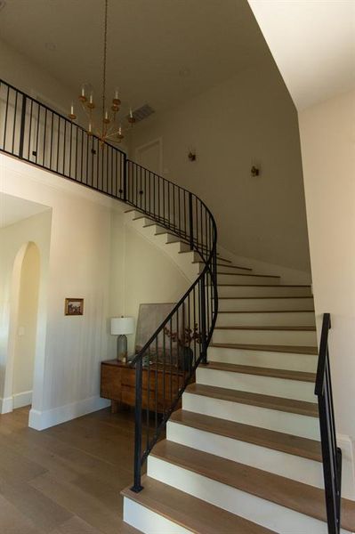 Stairway featuring wood finished floors, arched walkways, hanging lights, and a high ceiling