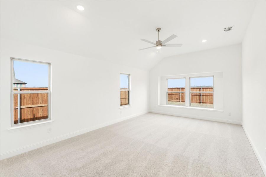 Empty bedroom with vaulted ceiling, ceiling fan, carpet flooring, and multiple windows Empty bedroom with vaulted ceiling, ceiling fan, carpet flooring, and multiple windows
