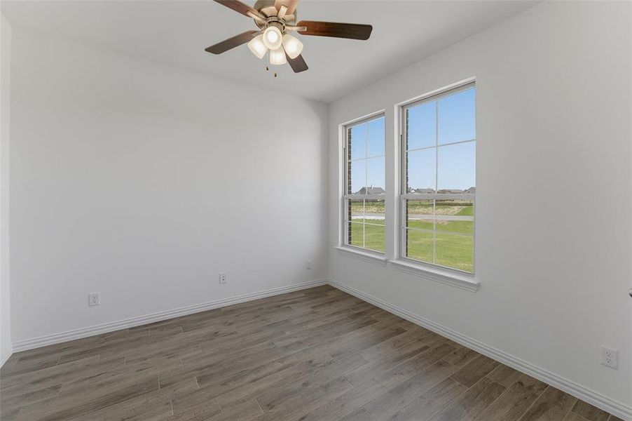Room featuring two large windows, wood-finish flooring, white baseboards, and a ceiling fan with integrated lighting