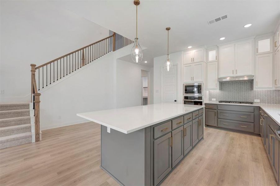 Two tone kitchen featuring dual tone cabinetry, light wood-style floors, hanging light fixtures, decorative backsplash, and glass fronted cabinets