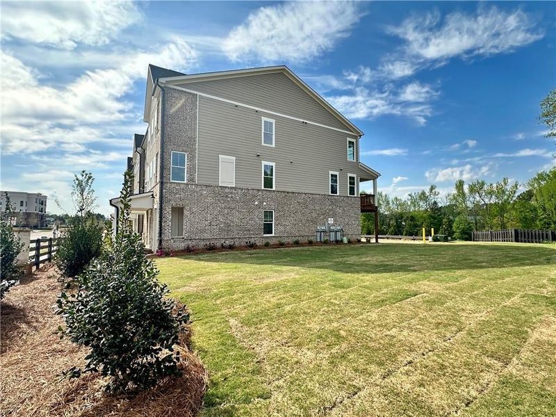 View of side of home featuring a yard, fence, and brick siding