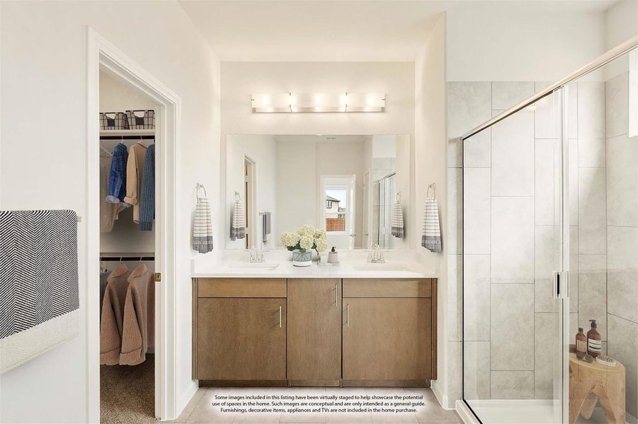 Ensuite bathroom with double vanity, wood cabinets, glass shower, and walk-in closet visible through doorway Ensuite bathroom with double vanity, wood cabinets, glass shower, and walk-in closet visible through doorway