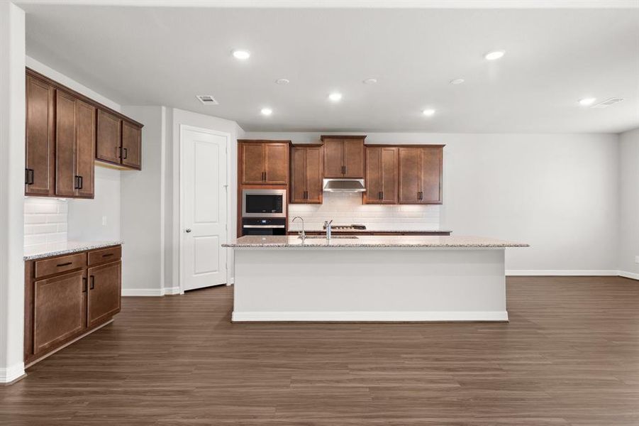 This light and bright kitchen features a large granite island, dark stained cabinets, a large sink overlooking your family room, recessed lighting, and beautiful backsplash.