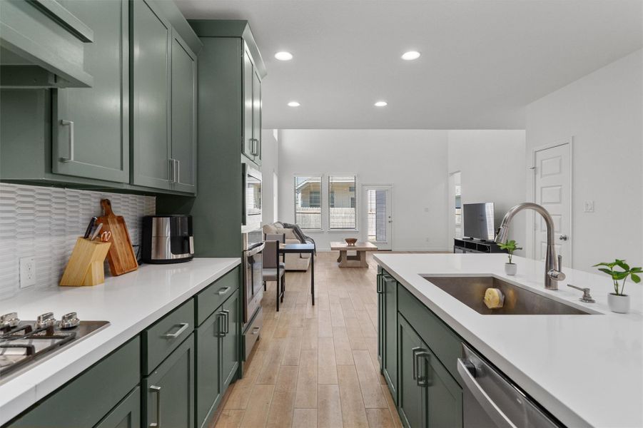 Kitchen with green cabinets, range hood, recessed lighting, stainless steel appliances, and light wood-style flooring