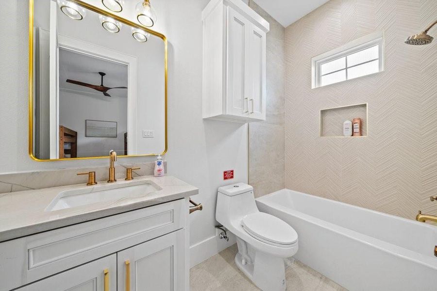 This stylish full bath features sleek gold hardware, elegant lighting, and a herringbone-tiled shower wall with built-in niche. A sophisticated space that perfectly blends function and design for guests or everyday use.