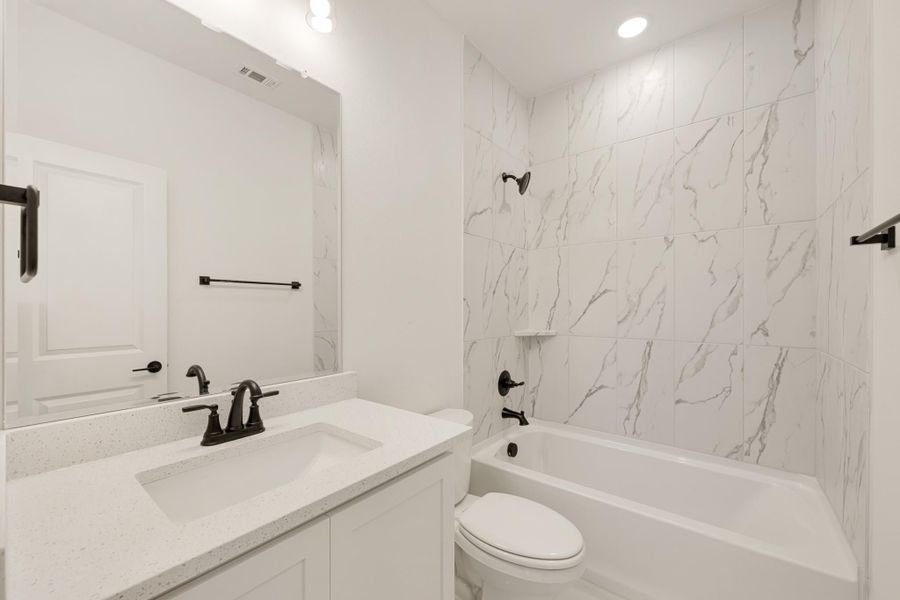 Bathroom with white quartz vanity, marble-look tile tub surround, and matte black fixtures